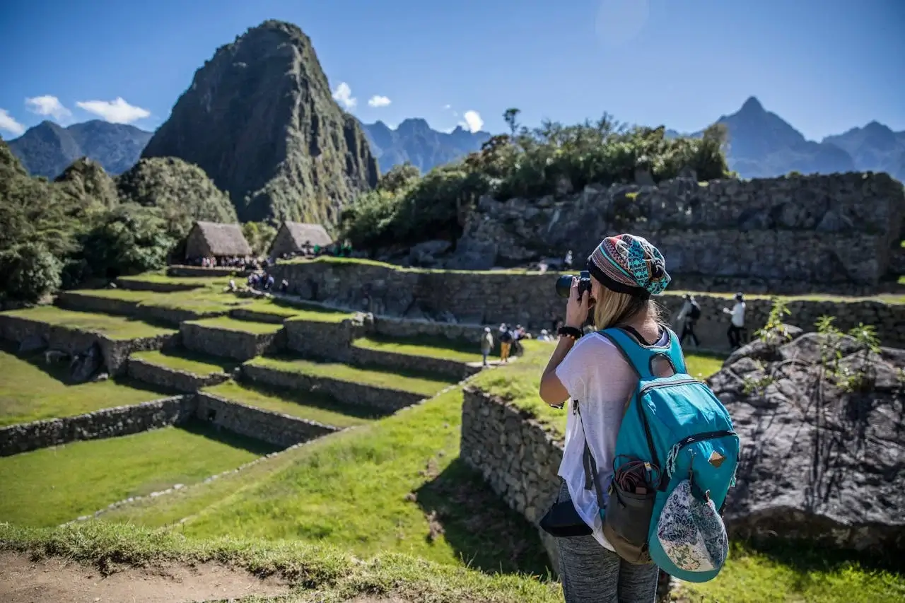 A sunny day in Machu Picchu with a tourist admiring the ancient ruins and stunning mountain backdrop. | Peruvian Sunrise