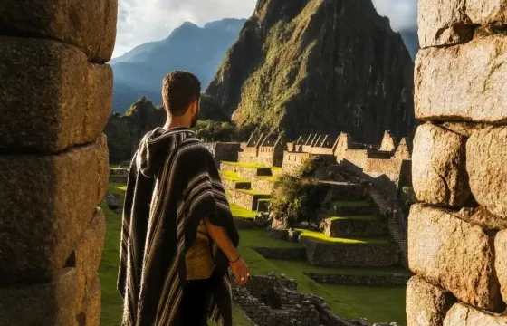 A sunny day in Machu Picchu with a tourist admiring the ancient ruins and stunning mountain backdrop. | Peruvian Sunrise